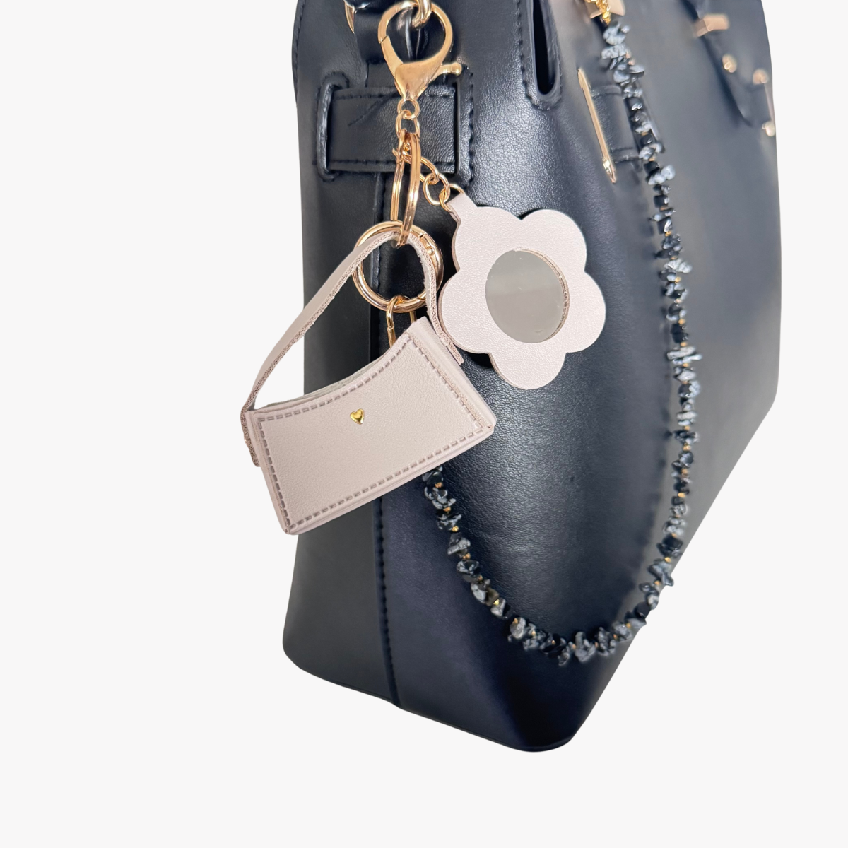 Black handbag with a flower-shaped keychain and beige cardholder on a white background