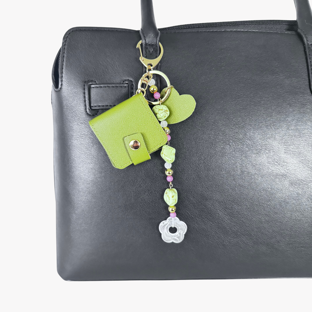 Green heart-shaped keychain with beads hanging from a black handbag.