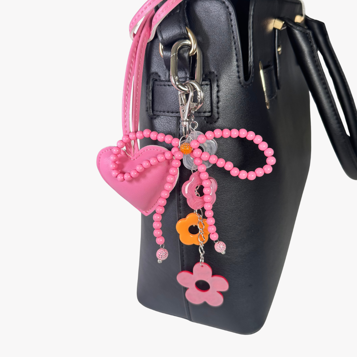 Pink heart-shaped keychain with beads and flowers attached to a black handbag.